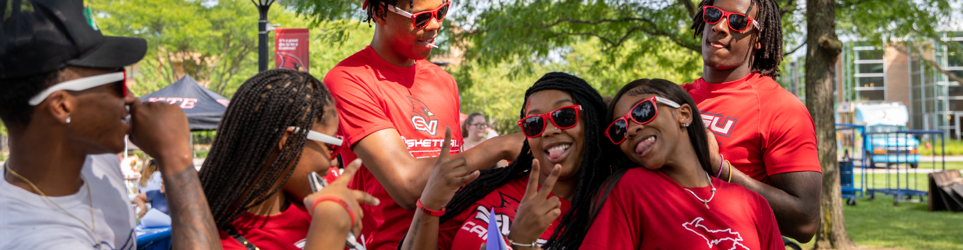 Students posing for a photo together at the SVSU Red Pride Picnic wearing SVSU Sunglasses and showing the peace sign.